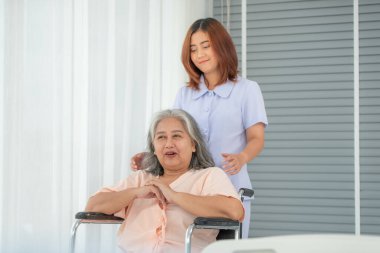 Hastane koğuşunda yaşlı kadın hastayı tekerlekli sandalyeye iten Asyalı hemşire, yaşlı bakım konsepti