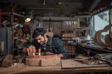 Luthier bir gitar yaratıyor ve geleneksel olarak aletleri kullanıyor. Yapım aşamasında olan bir gitarın gövdesine kelepçe takıyor. Yapıştırıcı yapışkanlığını geliştiriyor.