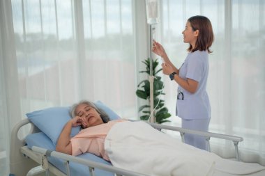 Asyalı hemşire hastane, sağlık ve sağlık hizmetlerinde kıdemli kadın hasta için serum torbası takıyor.