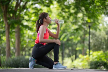 Attractive young Asian runner woman drinking water on road when she finished running training, after a workout