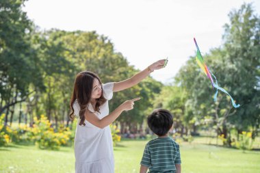 Mutlu Asyalı bir aile, eğlenceli bir anne ve oğlu parkta uçurtmayla oynuyor.