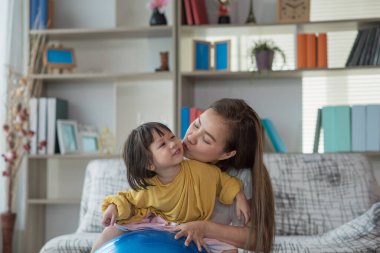 Mutlu Asyalı çocuk jimnastik topuyla eğleniyor, annesiyle evde egzersiz yapıyor.