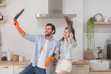 Genç mutlu çift mutfak temizliği yaparken eğleniyorlar paçavraları ellerinde tutuyorlar ve mutlu bir şekilde dans ediyorlar, mutlu aile kavramı.