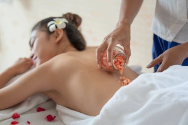 Genç Asyalı kadın spa salonundan zevk alıyor güzellik terapisti sağlık merkezindeki kadına tuz banyosu yaptırıyor, temizlik ve cilt bakımı konsepti uyguluyor.