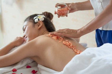 Genç Asyalı kadın spa salonundan zevk alıyor güzellik terapisti sağlık merkezindeki kadına tuz banyosu yaptırıyor, temizlik ve cilt bakımı konsepti uyguluyor.
