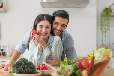 Mutlu çift evde yemek hazırlıyor, tezgahta taze sebze salatası, aşık erkek ve kadın.