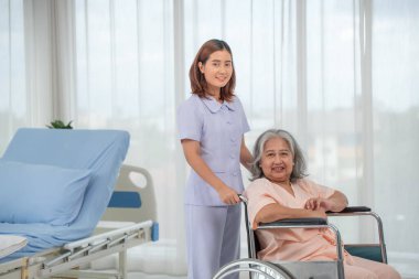 Hastane koğuşunda yaşlı kadın hastayı tekerlekli sandalyeye iten Asyalı hemşire, yaşlı bakım konsepti