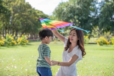 Mutlu Asyalı bir aile, eğlenceli bir anne ve oğlu parkta uçurtmayla oynuyor.