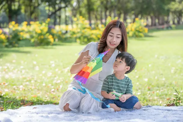 Mutlu Asyalı bir aile, eğlenceli bir anne ve oğlu parkta uçurtmayla oynuyor.