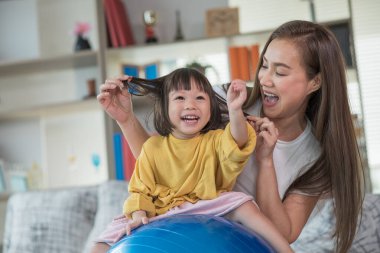 Mutlu Asyalı çocuk jimnastik topuyla eğleniyor, annesiyle evde egzersiz yapıyor.