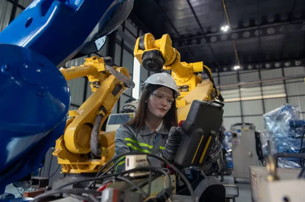 Robotik kol ve işletim makinesinin yanında duran miğfer güvenlikli mühendis. Teknisyen, tamir onarım elektronik işlemleri için kontrol ediyor.