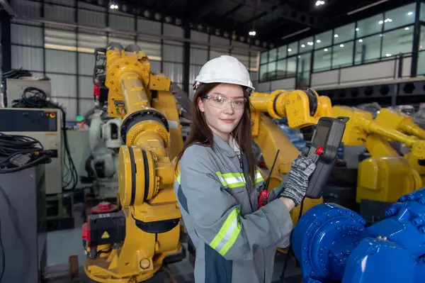 Robotik kol ve işletim makinesinin yanında duran miğfer güvenlikli mühendis. Teknisyen, tamir onarım elektronik işlemleri için kontrol ediyor.