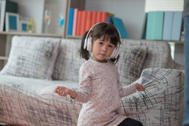 Mutlu Asyalı çocuk kulaklıkla müzik dinlerken ve bir odada dans ederken eğleniyor. Aktif eğlence ve yaşam tarzı kavramı.