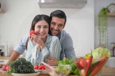 Mutlu çift evde yemek hazırlıyor, tezgahta taze sebze salatası, aşık erkek ve kadın.