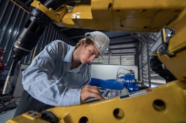 Robotik kol ve işletim makinesinin yanında duran miğfer güvenlikli mühendis. Teknisyen, tamir onarım elektronik işlemleri için kontrol ediyor.
