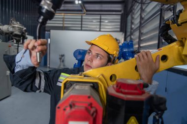 Robotik kol ve işletim makinesinin yanında duran miğfer güvenlikli mühendis. Teknisyen, tamir onarım elektronik işlemleri için kontrol ediyor.