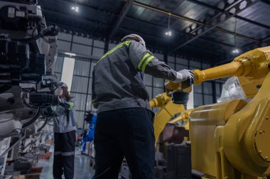 Robotik kol ve işletim makinesinin yanında duran miğfer güvenlikli mühendis. Teknisyen, tamir onarım elektronik işlemleri için kontrol ediyor.