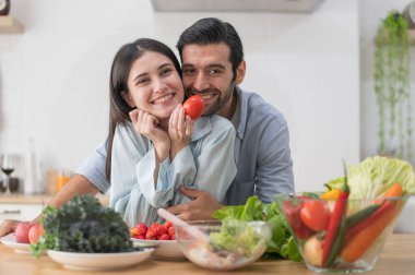 Mutlu çift evde yemek hazırlıyor, tezgahta taze sebze salatası, aşık erkek ve kadın.