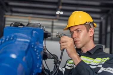 Robotik kol ve işletim makinesinin yanında duran miğfer güvenlikli mühendis. Teknisyen, tamir onarım elektronik işlemleri için kontrol ediyor.