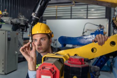 Robotik kol ve işletim makinesinin yanında duran miğfer güvenlikli mühendis. Teknisyen, tamir onarım elektronik işlemleri için kontrol ediyor.