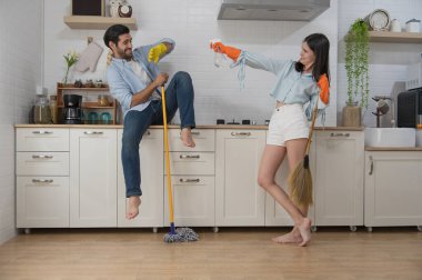 Mutfağı temizleyen mutlu genç çift ellerinde sprey şişeyle paspas ve paçavralar tutuyorlar. Mutlu aile kavramı.