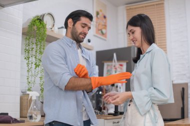 Gaz sobasını temizlemek için mutfakta lastik koruyucu eldivenler giyen genç çift bez ve etkili temizlik ürünleri kullanıyor. Mutlu aile kavramı.