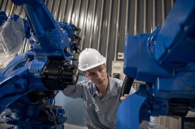 Robotik kol ve işletim makinesinin yanında duran miğfer güvenlikli mühendis. Teknisyen, tamir onarım elektronik işlemleri için kontrol ediyor.