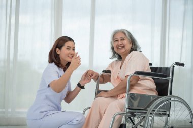 Klinikte ya da hastanede yaşlı bir kadının elini tutan gülümseyen Asyalı doktor, yaşlıların sağlık hizmetleri kavramı