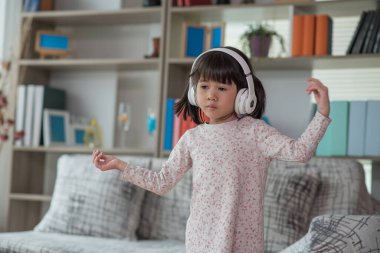 Mutlu Asyalı çocuk kulaklıkla müzik dinlerken ve bir odada dans ederken eğleniyor. Aktif eğlence ve yaşam tarzı kavramı.