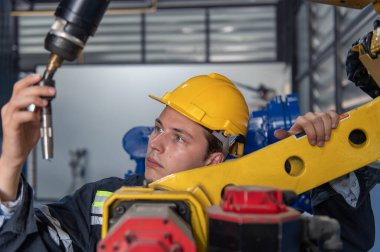 Robotik kol ve işletim makinesinin yanında duran miğfer güvenlikli mühendis. Teknisyen, tamir onarım elektronik işlemleri için kontrol ediyor.
