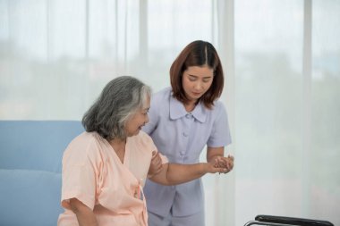 Hastane koğuşunda yaşlı kadın hastayı tekerlekli sandalyeye iten Asyalı hemşire, yaşlı bakım konsepti