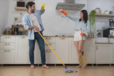 Mutfağı temizleyen mutlu genç çift ellerinde sprey şişeyle paspas ve paçavralar tutuyorlar. Mutlu aile kavramı.