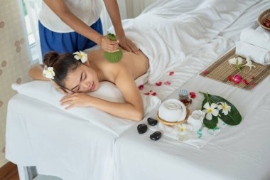 Genç Asyalı kadın spa salonunda Tayland bitkisel toplarıyla masaj yaptırıyor.