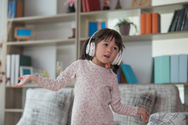 Mutlu Asyalı çocuk kulaklıkla müzik dinlerken ve bir odada dans ederken eğleniyor. Aktif eğlence ve yaşam tarzı kavramı.