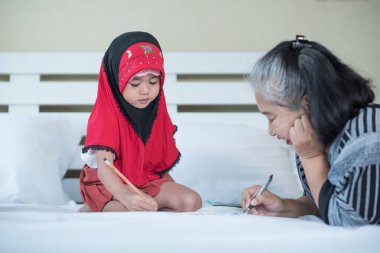 Genç Müslüman kız büyükannesiyle kitap yazıyor. Küçük İslami çocuk evde ödev yapıyor.