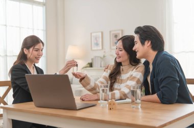 Emlakçı ev anahtarlarını müşteriye veriyor. Asyalı kadın emlakçı ev modeliyle aynı masada otururken alıcıya anahtarları veriyor. Gayrimenkul, yeni mülk alımı, ipotek konsepti
