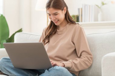 Konsantre olmuş Asyalı kız hafta sonu evde dizüstü bilgisayarda çalışıyor, internette kablosuz internet alışverişi yapmakla meşgul.