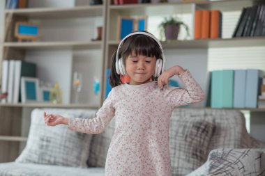 Mutlu Asyalı çocuk kulaklıkla müzik dinlerken ve bir odada dans ederken eğleniyor. Aktif eğlence ve yaşam tarzı kavramı.
