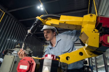 Robotik kol ve işletim makinesinin yanında duran miğfer güvenlikli mühendis. Teknisyen, tamir onarım elektronik işlemleri için kontrol ediyor.