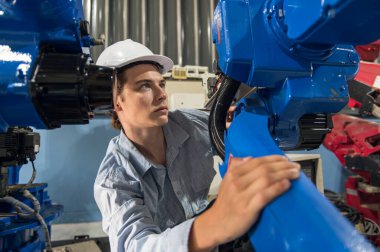 Robotik kol ve işletim makinesinin yanında duran miğfer güvenlikli mühendis. Teknisyen, tamir onarım elektronik işlemleri için kontrol ediyor.