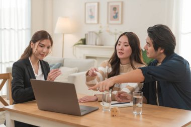 Asyalı finans danışmanı ofisteki genç çifte yeni proje yatırımını açıklıyor. Emlakçı aileyle ipotek seçeneklerini tartışıyor. Finans danışmanıyla ipotek kredisi danışmanlığı.