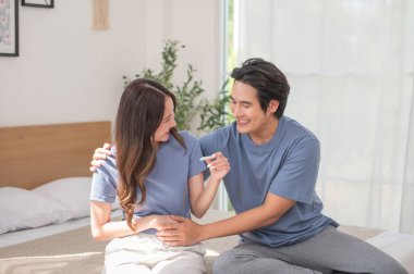 Asyalı çift, çocuklarını evde test ederken mutlu oluyor. Erkek ve kadın, gelecekte anne ve baba olmak için mutlulukla gülümsüyor. Aile ilişkileri kavramı.