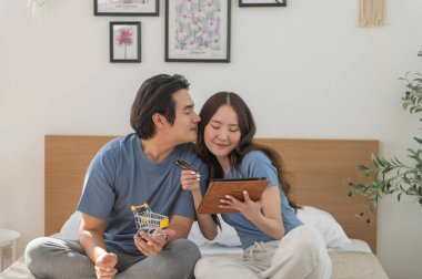 Genç Asyalı çift evde dijital tablet kullanırken online alışveriş yaparken, çift fatura ödemek için kredi kartı kullanıyor veya tatil için bir oda ayırtıyor, internette geziniyor ve online alışveriş yapıyor.