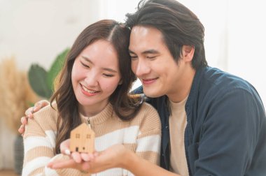 Mutlu Asyalı aile genç çiftimiz ellerinde model evlerle yeni bir ev almak için para biriktirmenin anahtarlarını gösteriyorlar. İş finansmanı, finansal planlama için banka mevduatı.
