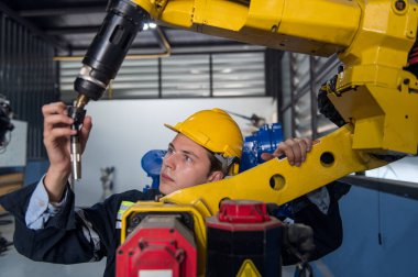 Robotik kol ve işletim makinesinin yanında duran miğfer güvenlikli mühendis. Teknisyen, tamir onarım elektronik işlemleri için kontrol ediyor.