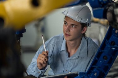 Robotik kol ve işletim makinesinin yanında duran miğfer güvenlikli mühendis. Teknisyen, tamir onarım elektronik işlemleri için kontrol ediyor.