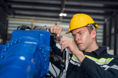 Robotik kol ve işletim makinesinin yanında duran miğfer güvenlikli mühendis. Teknisyen, tamir onarım elektronik işlemleri için kontrol ediyor.