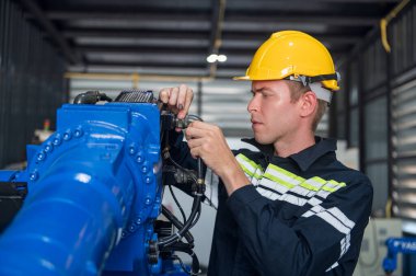 Robotik kol ve işletim makinesinin yanında duran miğfer güvenlikli mühendis. Teknisyen, tamir onarım elektronik işlemleri için kontrol ediyor.