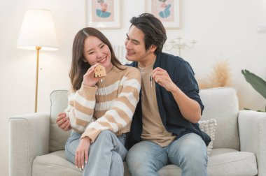 Mutlu Asyalı aile genç çiftimiz ellerinde model evlerle yeni bir ev almak için para biriktirmenin anahtarlarını gösteriyorlar. İş finansmanı, finansal planlama için banka mevduatı.