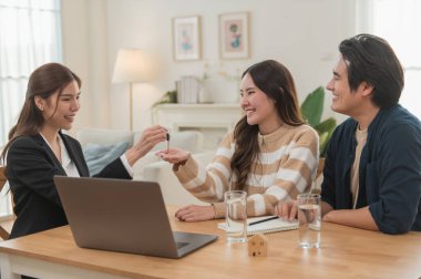 Emlakçı ev anahtarlarını müşteriye veriyor. Asyalı kadın emlakçı ev modeliyle aynı masada otururken alıcıya anahtarları veriyor. Gayrimenkul, yeni mülk alımı, ipotek konsepti